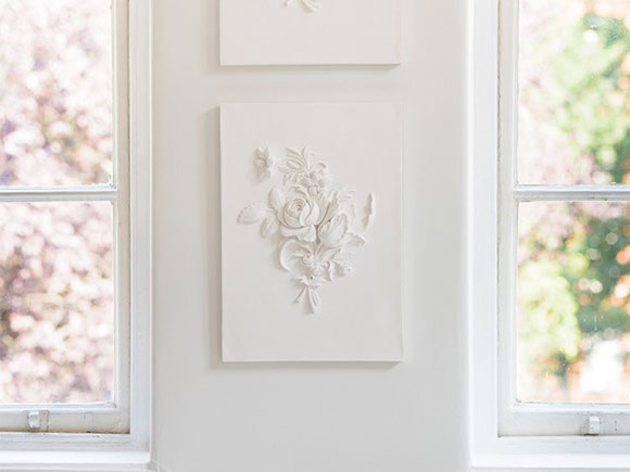 Photo of white plaster 3D artwork by Geoffrey Preston of a posy of flowers, displayed on wall in Helen Amy Murray studio